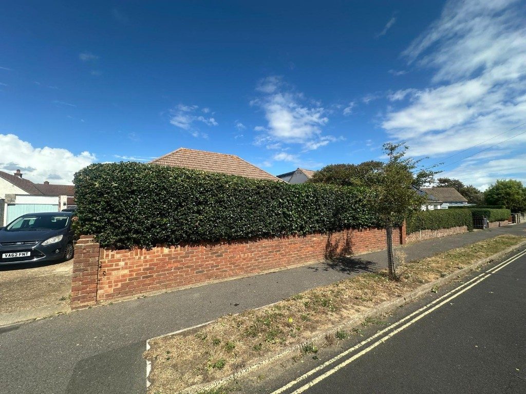 A roadside hedge cut flat and level along the top of a brick wall in Hampshire